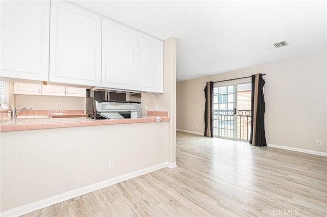 kitchen with tile countertops, visible vents, white cabinets, and stove