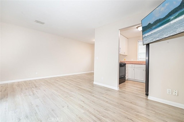 unfurnished living room featuring light wood-type flooring, visible vents, and baseboards