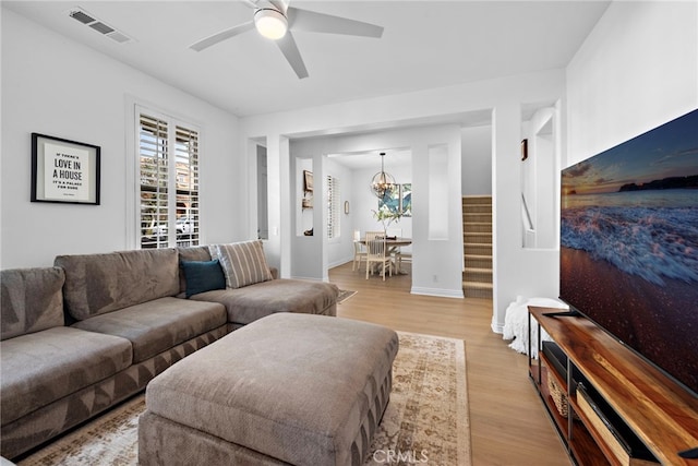 living room featuring ceiling fan with notable chandelier and light hardwood / wood-style floors