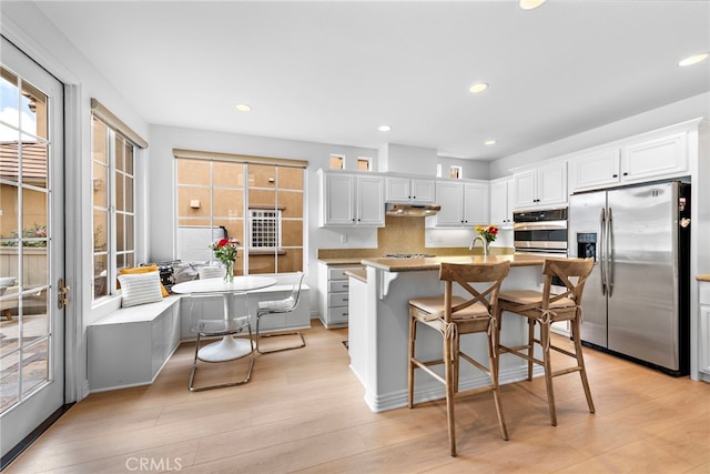 kitchen featuring appliances with stainless steel finishes, a kitchen bar, an island with sink, and white cabinets