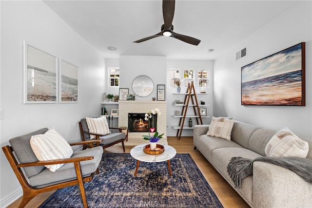 living room with a brick fireplace, hardwood / wood-style flooring, and ceiling fan