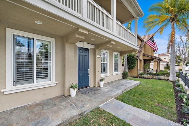 view of exterior entry with a balcony and a lawn