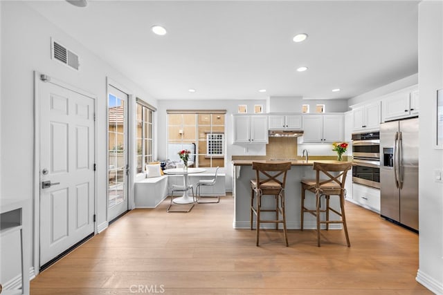 kitchen featuring a kitchen bar, white cabinetry, a center island, appliances with stainless steel finishes, and light hardwood / wood-style floors