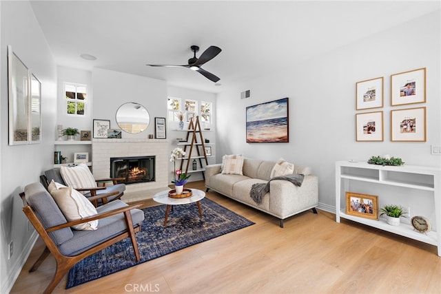 living room with ceiling fan, light hardwood / wood-style floors, and a brick fireplace