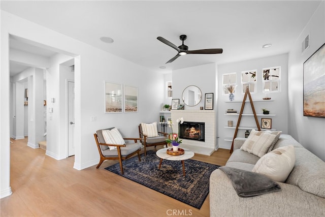 living room with ceiling fan, a fireplace, and light hardwood / wood-style flooring