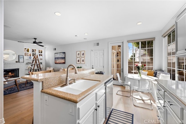 kitchen featuring sink, stainless steel dishwasher, an island with sink, a fireplace, and white cabinets