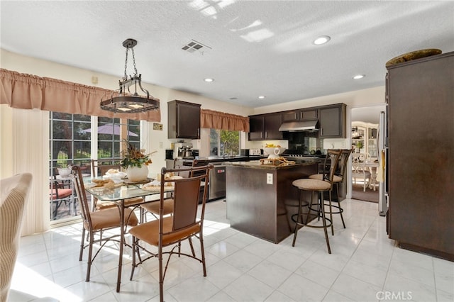 kitchen with hanging light fixtures, a center island, dark brown cabinetry, light tile patterned floors, and a textured ceiling