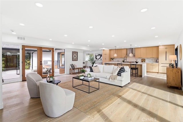 living room with a healthy amount of sunlight, light hardwood / wood-style floors, and french doors