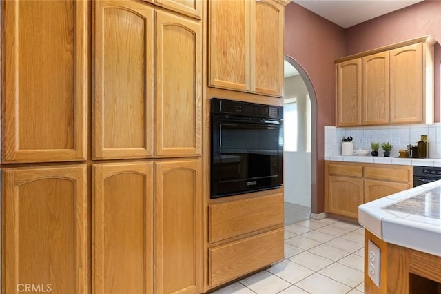 kitchen featuring tile counters, light tile patterned floors, backsplash, and black oven