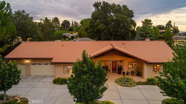 view of front of property featuring driveway, a tiled roof, an attached garage, and stucco siding