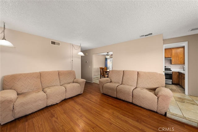 living room featuring ceiling fan, light hardwood / wood-style floors, and a textured ceiling