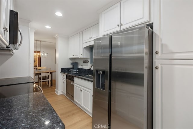 kitchen featuring light wood finished floors, dark stone counters, stainless steel appliances, white cabinetry, and a sink