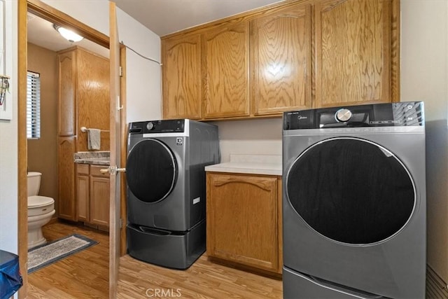 clothes washing area with washing machine and dryer, cabinets, and light hardwood / wood-style flooring