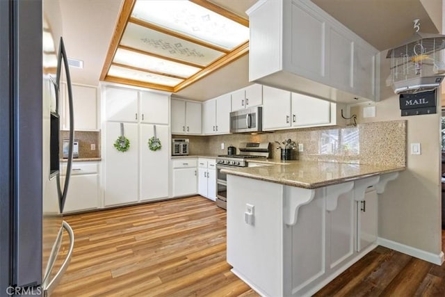 kitchen with white cabinetry, kitchen peninsula, stone counters, and stainless steel appliances