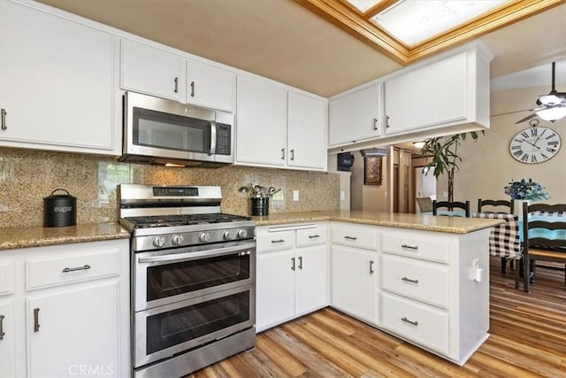 kitchen with appliances with stainless steel finishes, light hardwood / wood-style flooring, backsplash, white cabinetry, and kitchen peninsula