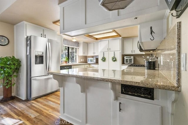 kitchen with white cabinets, kitchen peninsula, light stone counters, and stainless steel fridge with ice dispenser