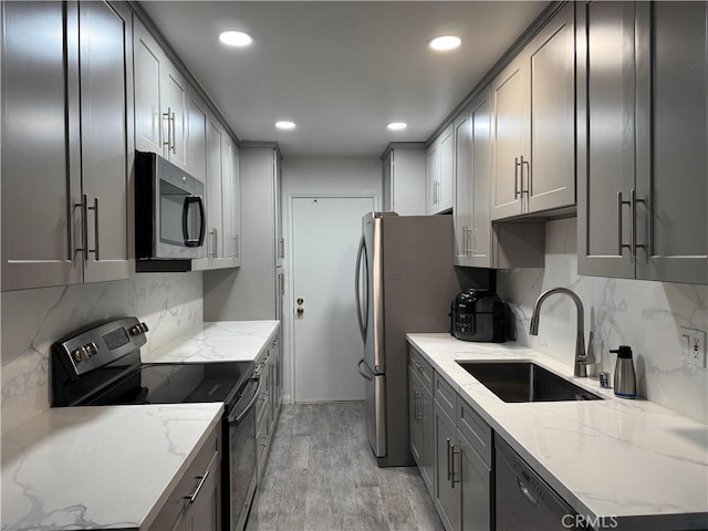 kitchen featuring light stone counters, stainless steel appliances, a sink, light wood-style floors, and gray cabinets