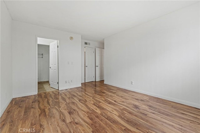 unfurnished bedroom with a spacious closet, wood finished floors, visible vents, and baseboards