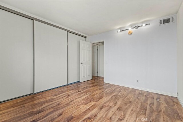 empty room featuring wood finished floors, visible vents, and baseboards