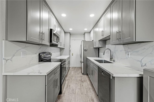 kitchen with light wood-type flooring, decorative backsplash, gray cabinets, appliances with stainless steel finishes, and a sink