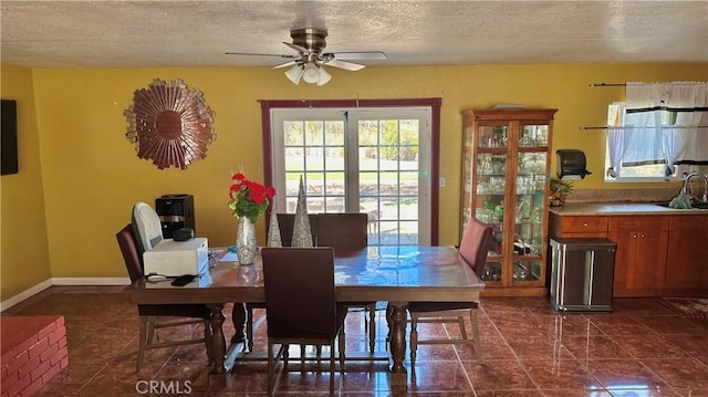 dining space featuring dark tile patterned flooring, baseboards, a ceiling fan, and a textured ceiling