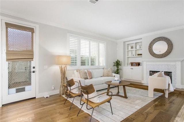 living room with built in features, ornamental molding, light hardwood / wood-style floors, and a premium fireplace