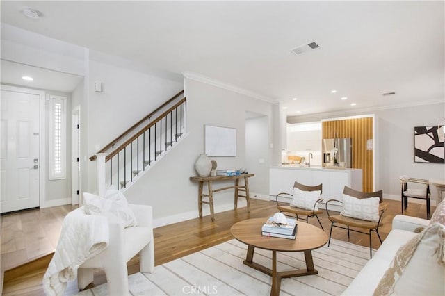 living room featuring sink, crown molding, and light hardwood / wood-style flooring