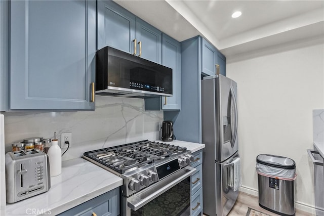 kitchen featuring light wood-style flooring, appliances with stainless steel finishes, light stone counters, blue cabinets, and backsplash