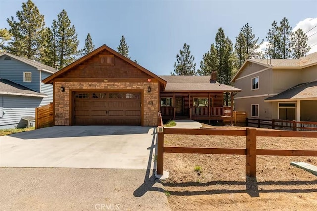 view of front facade featuring fence, driveway, stone siding, and an attached garage