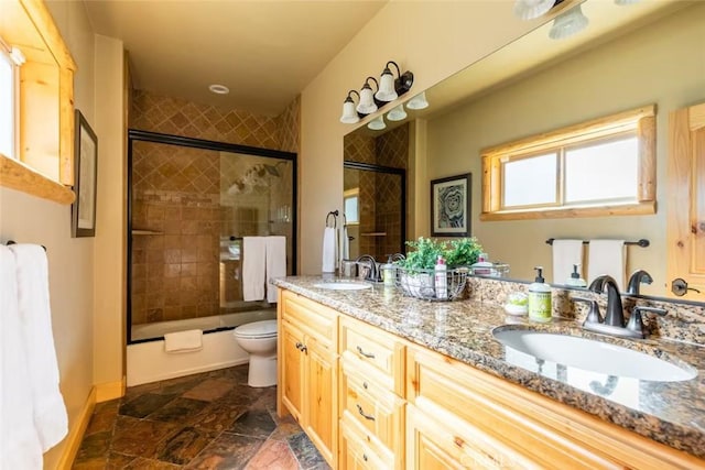 bathroom featuring toilet, a sink, double vanity, and bath / shower combo with glass door