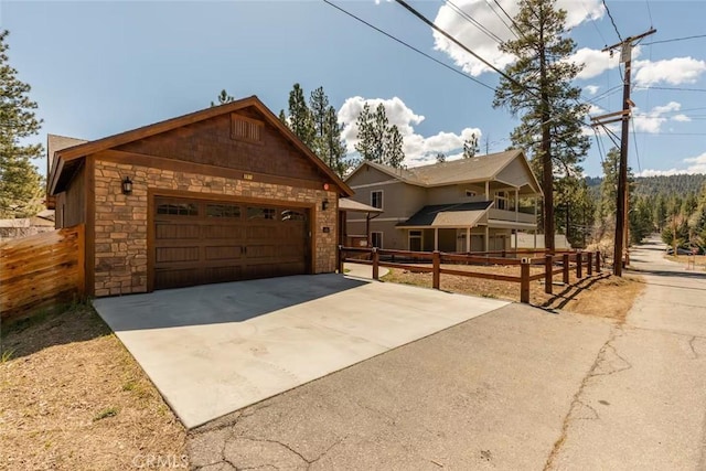 view of front facade with stone siding, concrete driveway, an attached garage, an outdoor structure, and fence