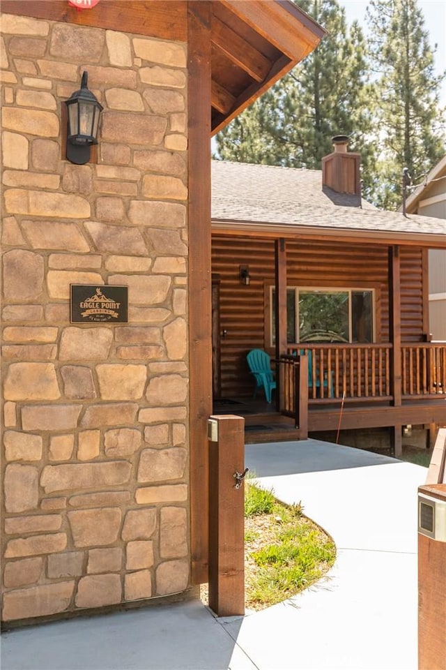 exterior space featuring covered porch, stone siding, roof with shingles, and a chimney