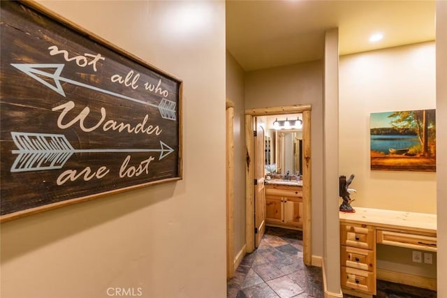 hallway with baseboards, stone finish flooring, and a sink
