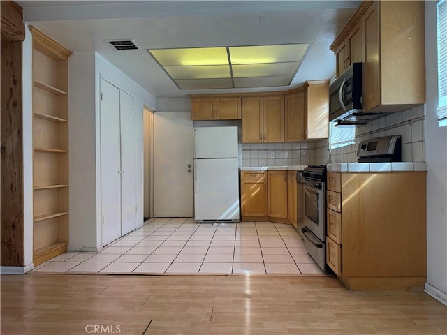 kitchen featuring tile counters, light wood-type flooring, stainless steel appliances, and decorative backsplash