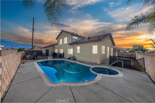 pool at dusk featuring a mountain view, a patio, a fenced backyard, and a pool with connected hot tub