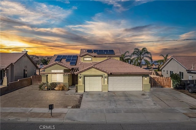 view of front facade with stucco siding, fence, a tile roof, and roof mounted solar panels