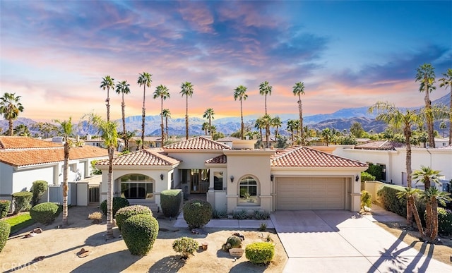 mediterranean / spanish house with an attached garage, a tiled roof, concrete driveway, and stucco siding