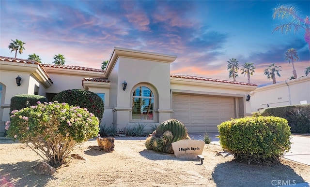 mediterranean / spanish-style house with concrete driveway, a tile roof, an attached garage, and stucco siding