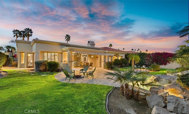 3 Mesquite Ridge Ln, Rancho Mirage, CA 92270 - back of house at dusk with a patio, a yard, stucco siding, and a chimney