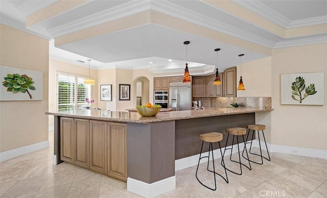 kitchen with appliances with stainless steel finishes, ornamental molding, a peninsula, a tray ceiling, and a kitchen bar