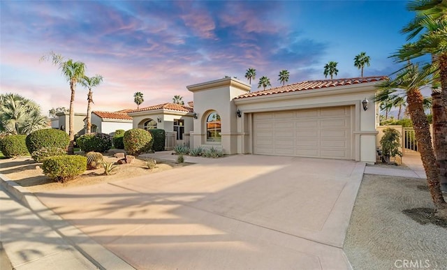 mediterranean / spanish house with a garage, concrete driveway, a tiled roof, and stucco siding