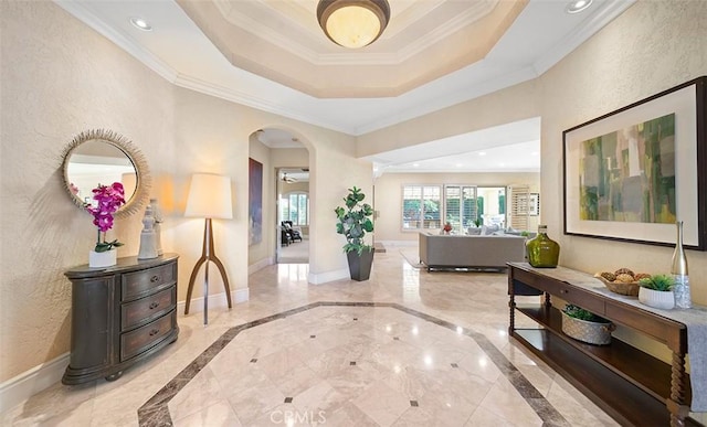 entrance foyer featuring arched walkways, crown molding, a raised ceiling, and baseboards