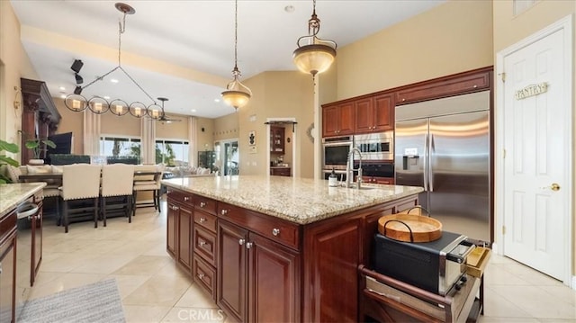 kitchen featuring a center island with sink, open floor plan, built in appliances, light stone countertops, and pendant lighting