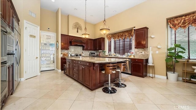 kitchen featuring light tile patterned floors, decorative backsplash, a kitchen island, light stone counters, and hanging light fixtures