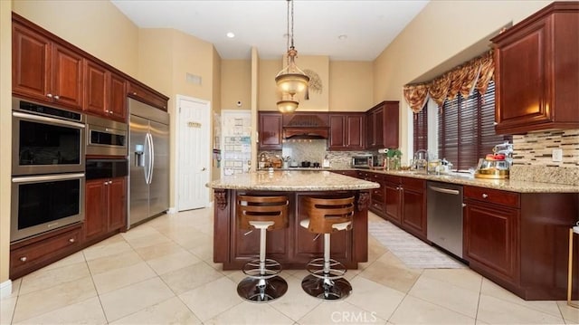 kitchen with stainless steel appliances, hanging light fixtures, light stone countertops, and a center island