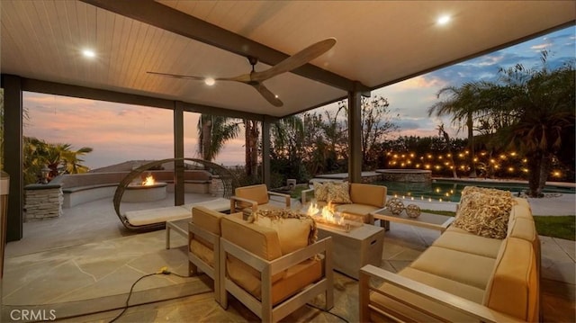 patio terrace at dusk featuring a pool with connected hot tub, a ceiling fan, and an outdoor living space with a fire pit