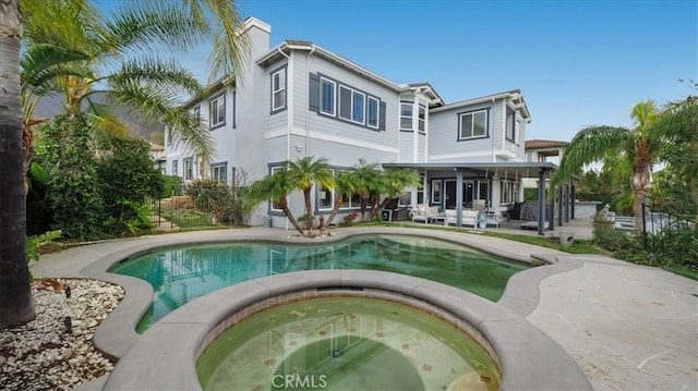 rear view of house with an outdoor pool, a patio, a sunroom, a chimney, and an in ground hot tub