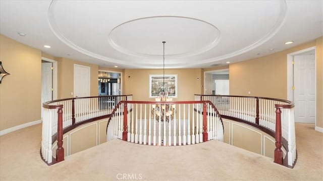 hallway featuring recessed lighting, a raised ceiling, an inviting chandelier, light carpet, and baseboards