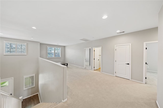 hallway featuring light carpet, an upstairs landing, visible vents, and baseboards