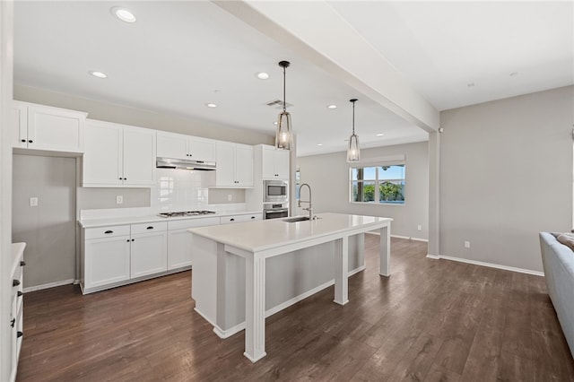 kitchen featuring visible vents, an island with sink, decorative light fixtures, light countertops, and under cabinet range hood